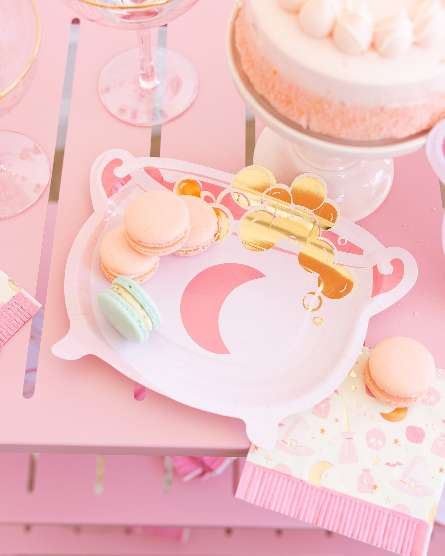 pink cauldron paper plates with a pink moon on front and gold foil bubbles on a table with macarons on top