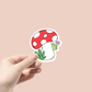 cute green frog hiding behind a red and white mushroom sticker