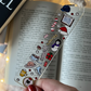 Decorative bookmark with Christmas-themed stickers held over an open book.