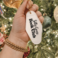 Hand holding a keychain with 'Silly Goose Book Club' text against a Christmas tree background